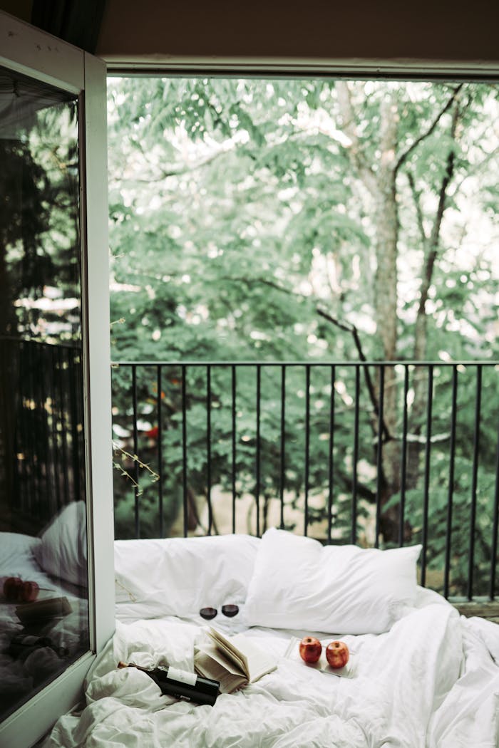 gallery-4 Comfortable bed and pillows with balcony view of lush green trees, creating a serene and relaxing ambiance.