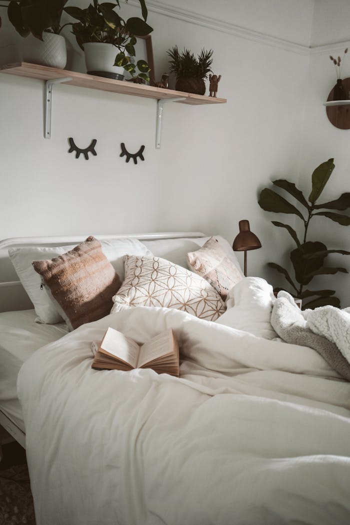 gallery-2 Warm and inviting bedroom setup with decorative pillows, plants, and an open book for a cozy ambiance.