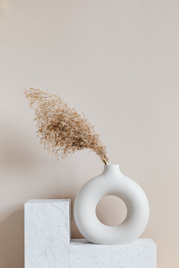 hero-img-01 Elegant ceramic vase with dried grass on a marble pedestal, showcasing simplicity and minimalism.