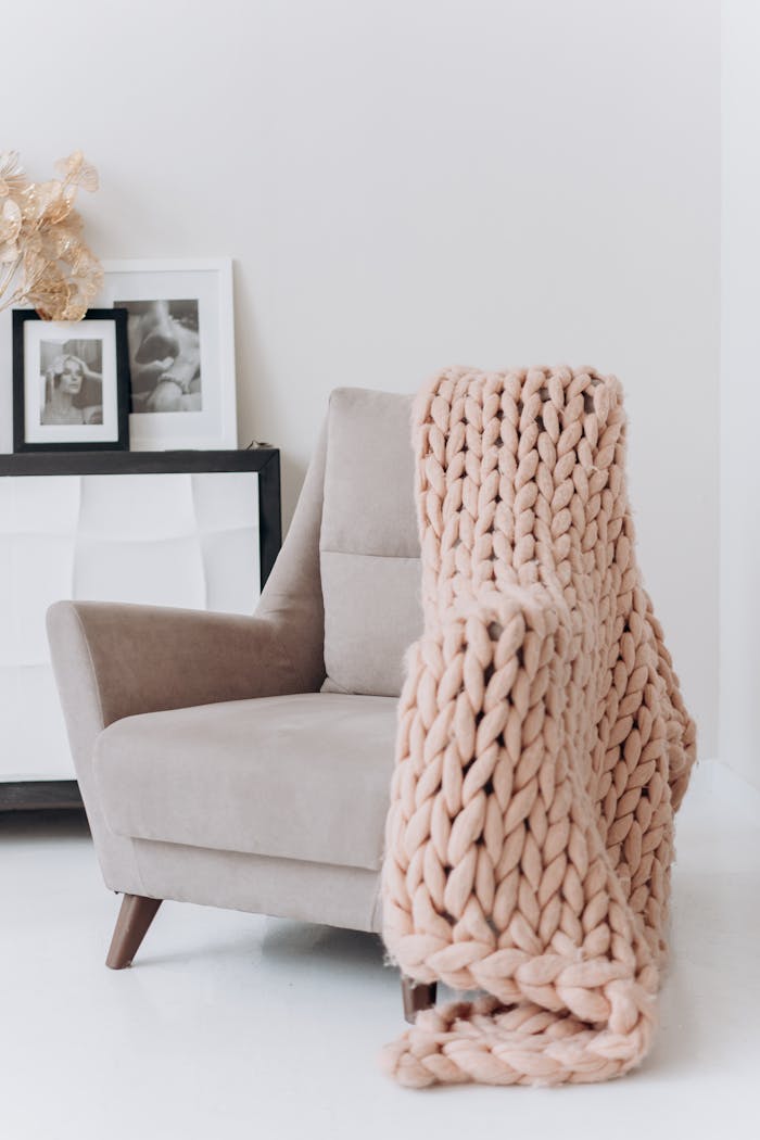 why-choose-us A modern beige armchair draped with a knitted throw blanket in a cozy interior setting.